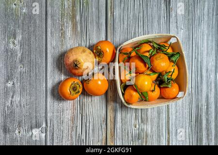 Top view image of basket of full ripe tangerines, some loose persimmons and a pomegranate on the wooden table Stock Photo