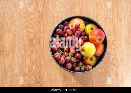 fruit bowl seen from the top with red grapes, red apples and pomegranate on oak colored background Stock Photo