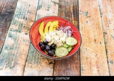 version of Greek salad with avocado, red onion, raw cucumbers with skin, black olives and diced feta cheese with Spanish olive oil Stock Photo