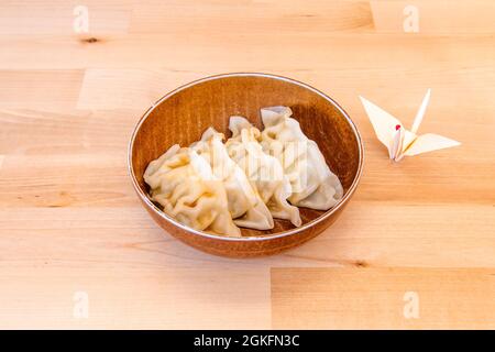 Typical Japanese dumplings steamed gyozas with an origami bird decorating on wooden table Stock Photo