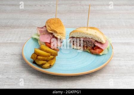 Beef burger with bacon and ham, tomato and lettuce cut in half with French fries on a blue plate Stock Photo