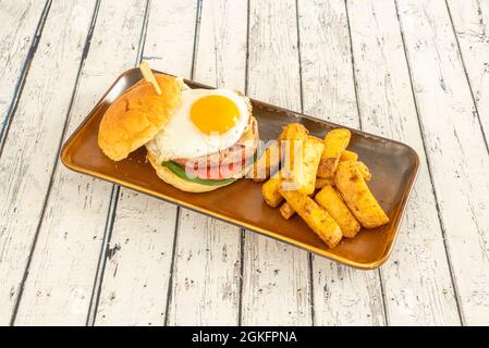 appetizing homemade burger with a fried egg with its shiny yolk and a side of deluxe fries with skin Stock Photo