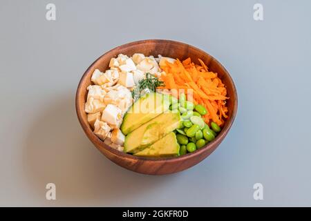 Vegan poke bowl recipe with tofu tacos, ripe avocado pieces, edamame beans with salt and filleted carrot with white rice base Stock Photo