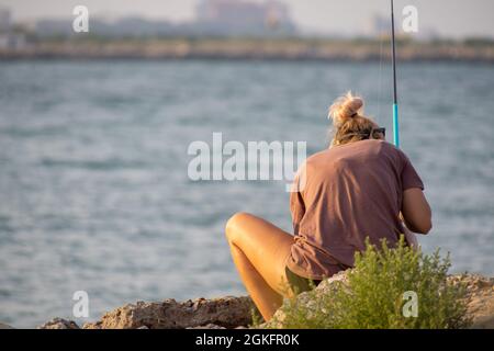 Woman sitting on a rock and tying to cath fish. Unrecognisable person. Stock Photo