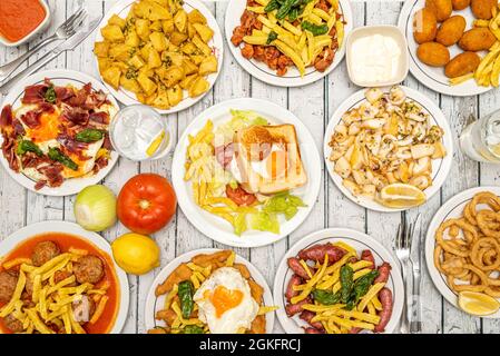 Top view of the table of a Spanish tapas restaurant with a sandwich with fried egg, meatloaf, homemade nuggets, scrambled eggs with ham, patatas brava Stock Photo