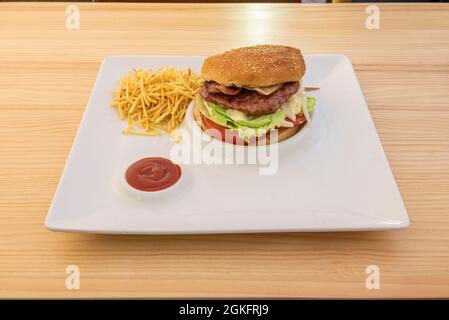 Classic hamburger with lettuce, tomato, onion, bacon, cheese and straw potatoes on white plate Stock Photo