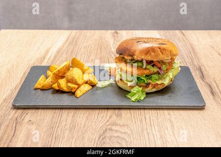 hamburger with chicken fillet battered with chopped onion and tomato, guacamole and lettuce among the toasted bread with a deluxe potato garnish on a Stock Photo