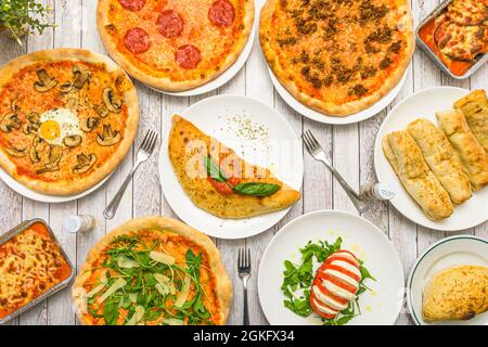 Typical Italian dishes on a restaurant table. Calzone, pizzas, capresse salad, meat lasagna and lots of arugula and basil Stock Photo