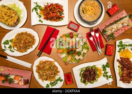 Sushi dishes and Chinese food. Assorted nigiri, sautéed noodles with shrimp, sautéed vegetables, udon noodles, lacquered duck, california roll, carame Stock Photo