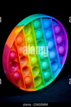 Rainbow coloured fidget popper toy to help relieve anxiety or sensory difficulties in children. Image is set against a black background Stock Photo