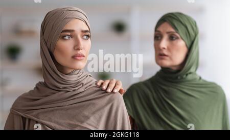 Senior Muslim Mother Touching Shoulder Of Unhappy Adult Daughter Indoor Stock Photo
