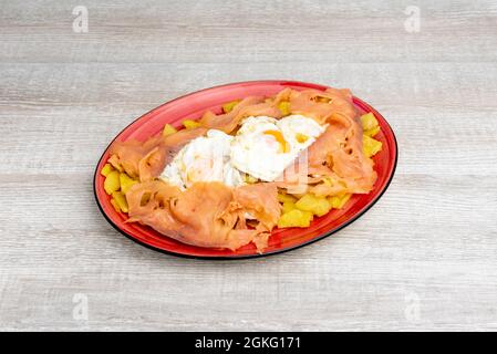 Red tray of fried eggs with smoked salmon slices on bed of chips on gray wooden table Stock Photo