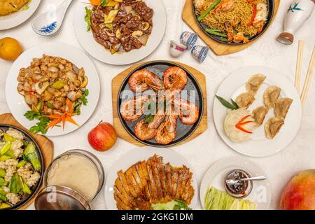 Top view image of popular Chinese restaurant dishes. Grilled prawns, steamed gyozas, Peking duck, chicken with almonds, veal with vegetables, sautéed Stock Photo
