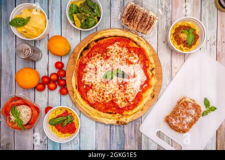 Top view image of typical Italian dishes with lots of basil, margarita pizza, tiramisu, bolognese noodles, cherry tomatoes, spaghetti, burrata, on woo Stock Photo