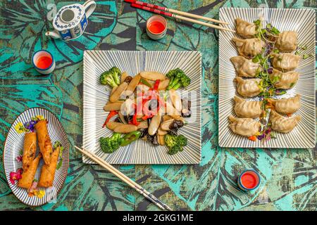 Top view image of Asian food dishes, shrimp rolls, steamed gyozas and rice pasta with vegetables and shiitake mushrooms Stock Photo
