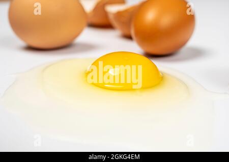 Close-up of raw broken egg showing yellow yolk and transparent white on white background Stock Photo