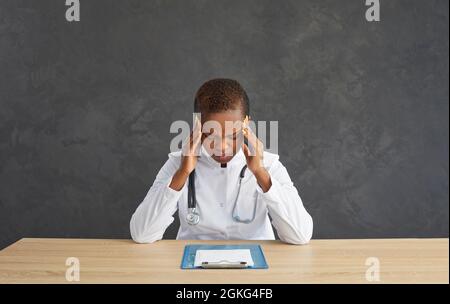 Tired young african american female doctor massaging temples feeling severe headache. Stock Photo
