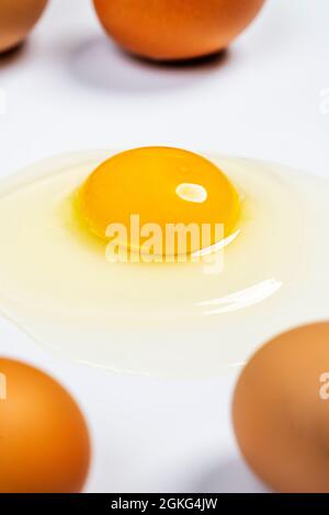 Cracked raw egg with yellow yolk and gleaming clear white on white table Stock Photo