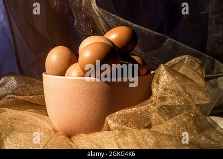 Pink bowl among tulle fabrics with gold glitters filled with fresh raw eggs Stock Photo
