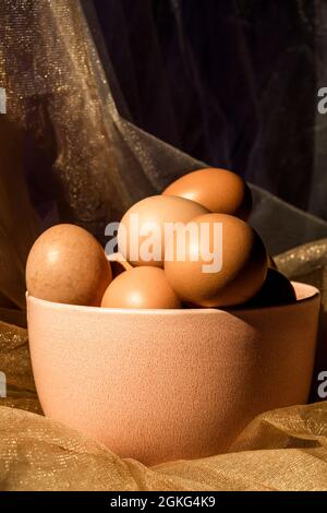 Pink bowl filled with brown chicken eggs on shiny brown tulle Stock Photo