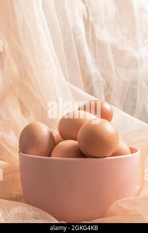 pink bowl full of raw eggs and background decorated with white and pink tulle fabric with glitters Stock Photo