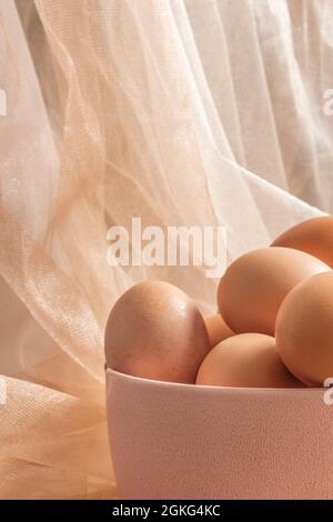 Pretty pink bowl with raw eggs and white and beige tulle fabric arrangements Stock Photo