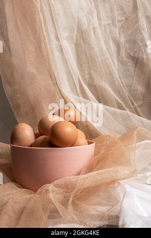 pink bowl with brown eggs on brown and white tulle cloth background Stock Photo