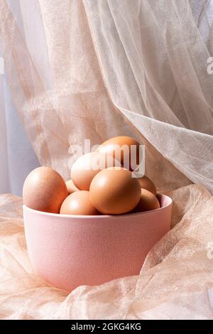 Pink bowl full of raw eggs surrounded by white and light brown tulle fabrics Stock Photo