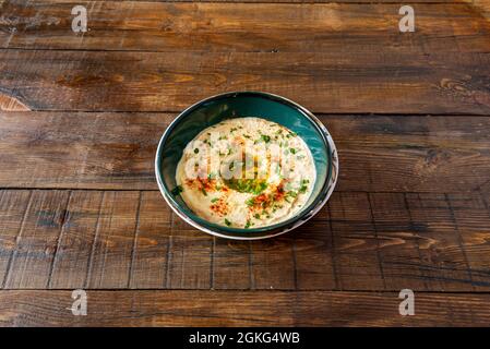 Fantastic Arabic chickpea hummus with olive oil, chopped parsley and paprika powder on the dark wooden table. Stock Photo