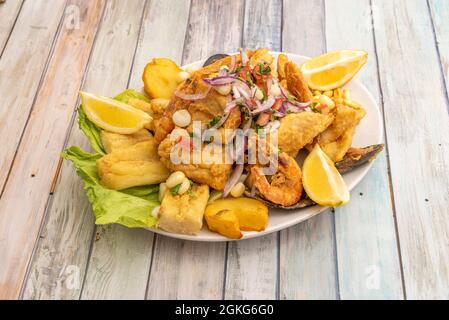 Popular recipe for Peruvian jelly with battered fried fish, fried prawns, yucca and French fries and red onion with corn and lemon wedges to garnish Stock Photo