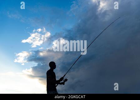 Salvador, Bahia, Brazil - April 18, 2021: Silhouette of fishermen with their poles at sunset. Stock Photo