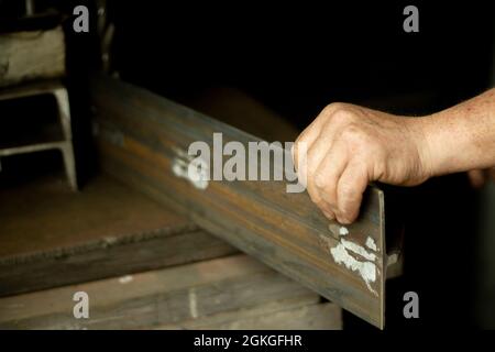 Worker with metal. The guy holds a steel part. Hard work in a metalworking workshop. Creation of steel construction. The working hands of a man. Stock Photo