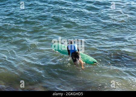 Salvador, Bahia, Brazil - June 17, 2021: Surfer entering the sea from Farol da Barra beach. Stock Photo