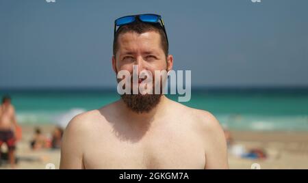 An authentic portrait of a young confident bearded man looking at the camera. Closeup side view of a young natural man on the beach. Stock Photo