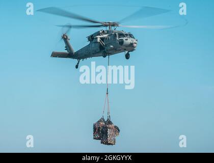 PACIFIC OCEAN (April 19, 2021) A U.S. Navy MH-60S Sea Hawk assigned to Helicopter Sea Combat Squadron 21 sling-loads cargo during a vertical replenishment-at-sea with amphibious transport dock ship USS Portland (LPD 27), April 19. The Marines and Sailors of the 11th MEU are conducting routine training as part of the Essex Amphibious Ready Group (ARG). Together, the 11th MEU, Amphibious Squadron (PHIBRON) 1, and ships are designated as an ARG. Stock Photo