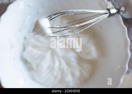 Whipped egg whites on mixer whisk. Process of cooking meringue. Baking dessert concept. Whipped egg whites - beaten italian meringue on a whisk Stock Photo