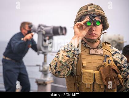 PACIFIC OCEAN (April 20, 2021) U.S. Marine Corps Lance Cpl. Zachary Hidalgo, a machine gunner with Weapons Company, Battalion Landing Team 1/1, 11th Marine Expeditionary Unit, provides observation during formation steaming aboard amphibious dock landing ship USS Pearl Harbor (LSD 52), April 20. The Marines and Sailors of the 11th MEU are conducting routine training as part of the Essex Amphibious Ready Group (ARG). Together, the 11th MEU, Amphibious Squadron (PHIBRON) 1, and ships are designated as an ARG. Stock Photo