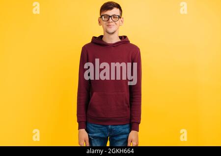 young guy in glasses and red sweater smiling cute on yellow background Stock Photo