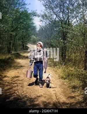1950s BOY WITH BEAGLE PUPPY WALKING DOWN COUNTRY ROAD WHISTLING CARRYING  FISHING POLE PAIL AND FISH - a2790c DEB001 HARS JUVENILE POLE FRIEND  VACATION PLEASED JOY SATISFACTION PROUD RURAL HOME LIFE COPY