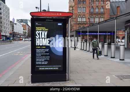 A man wearing a protective face mask walks past a Stay Home sign on a bus stop in King's Cross during the second national lockdown in England. London, United Kingdom 21 November 2020. Stock Photo