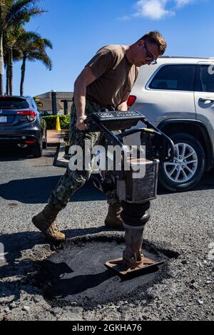 U.S. Navy Petty Officer 2nd Class Christopher Fike, advanced builder, base facilities, Marine Corps Base Hawaii, compacts asphalt into a pot hole, MCBH, April 22, 2021. Base facilities has been working to restore MCBH’s roadways one pot hole at a time. Stock Photo