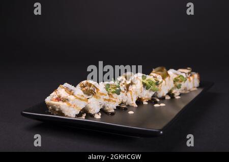 Closeup of bonito sushi rolls served on a black plate on a black background