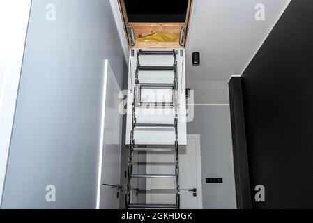 Metal stairs hidden in the ceiling to the attic with an opening hatch and folding stairs in the corridor, modern look. Stock Photo