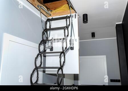 Metal stairs hidden in the ceiling to the attic with an opening hatch and folding stairs in the corridor, modern look. Stock Photo