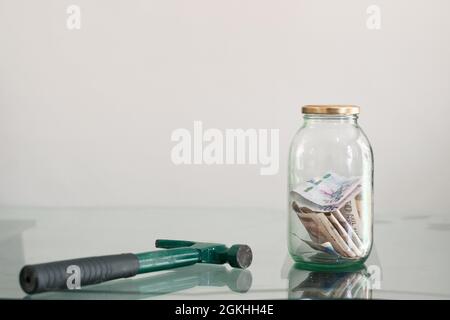hammer next to glass jar full of banknotes. hammer to break glass piggy bank. concept of economy and personal savings Stock Photo