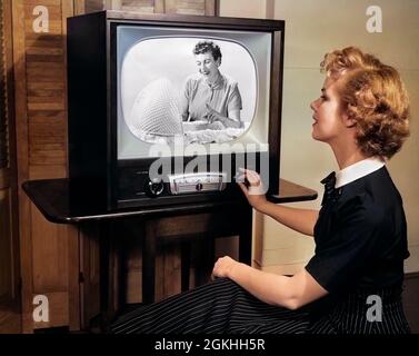 1950s BLONDE WOMAN TURNING DIAL ON TV SET WATCHING PROGRAM ABOUT BABY CHILDCARE - r3727c DEB001 HARS 1 APPLIANCE JUVENILE COMMUNICATION BLOND YOUNG ADULT INFORMATION PARENTING FEMALES RELATION STUDIO SHOT RELAX HOME LIFE LEARN COPY SPACE HALF-LENGTH ENTERTAINMENT B&W TELEVISIONS SINGULAR MATERNAL INTERESTING INTEREST BASSINET FEMININE RELATIONSHIPS KNOB PINSTRIPE INSTRUCTION MOTHERHOOD DEB001 REALITY CHILDCARE JUVENILES MOMS PARENTAL PARENTHOOD PROGRAM YOUNG ADULT WOMAN BLACK AND WHITE CAUCASIAN ETHNICITY OLD FASHIONED Stock Photo