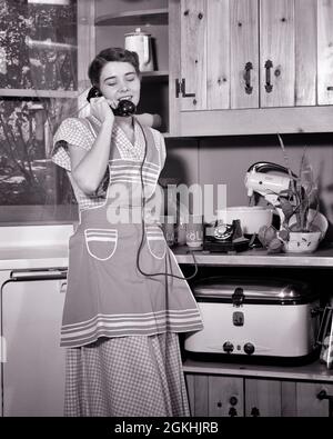 1940s 1950s SMILING WOMEN HOUSEWIFE IN KITCHEN WEARING APRON TALKING ON TELEPHONE SURROUNDED BY ELECTRONIC KITCHEN APPLIANCES - t1410 HAR001 HARS HOME LIFE COMMUNICATING COPY SPACE FULL-LENGTH HALF-LENGTH INSPIRATION CARING UNDERWATER CONFIDENCE B&W SUCCESS HOMEMAKER APPLIANCES CABINETS HAPPINESS HOMEMAKERS CHEERFUL LEISURE NETWORKING CHOICE EXCITEMENT KNOWLEDGE PROGRESS RECREATION SURROUNDED INNOVATION PRIDE BY IN ON OPPORTUNITY HOUSEWIVES PHONES SMILES CONNECTION CONCEPTUAL TELEPHONES JOYFUL STYLISH KNOTTY PINE ELECTRONIC GROWTH MID-ADULT MID-ADULT WOMAN RELAXATION ROASTER YOUNG ADULT WOMAN Stock Photo
