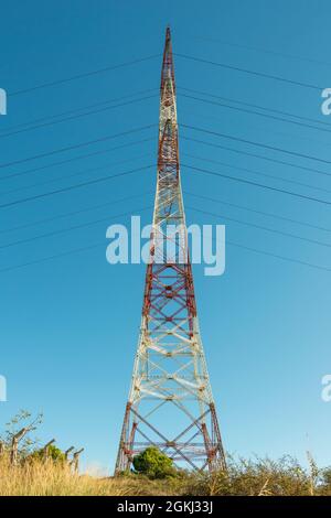 High tension steel tower painted in white and red loaded with electric cables with dry vegetation at the base Stock Photo