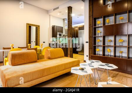 Living room and kitchen decorated in ocher and wood tones with yellow flowers and full-length gold mirror in a vacation rental apartment Stock Photo