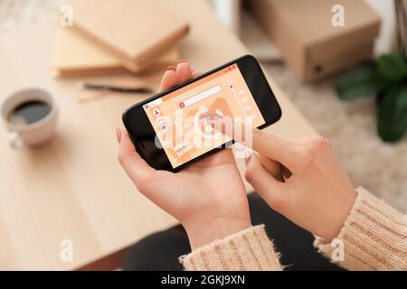 Woman using mobile phone with open page of delivery service application at home, closeup Stock Photo